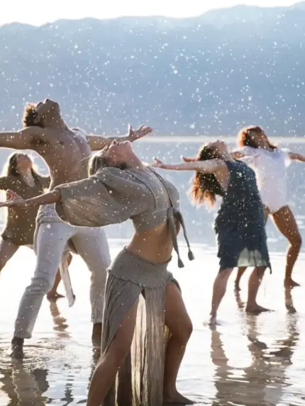 Danza grupal al aire libre, con varias personas moviéndose en conexión y expresión corporal consciente junto al agua.