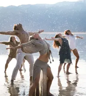 Danza grupal al aire libre, con varias personas moviéndose en conexión y expresión corporal consciente junto al agua.